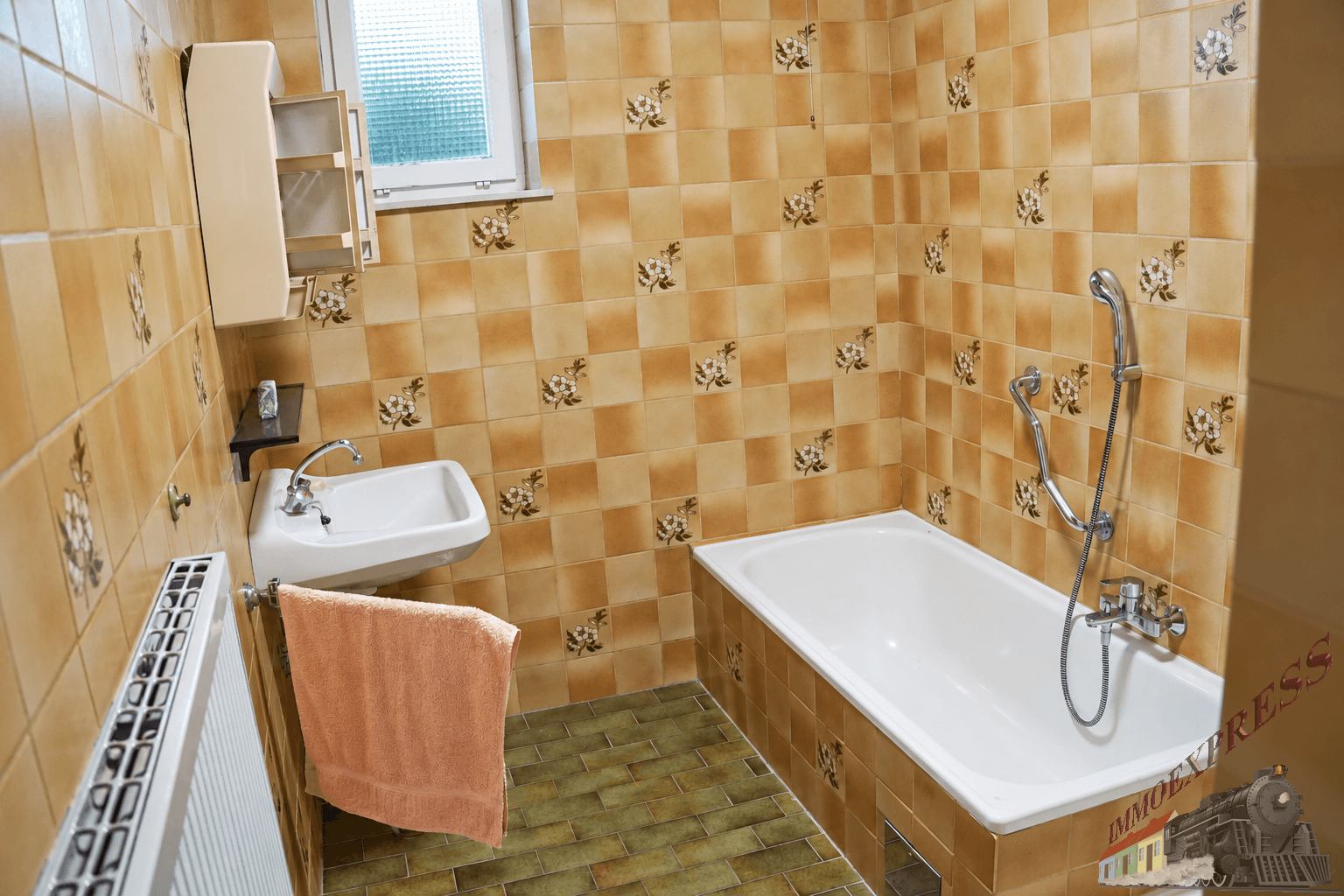 Badezimmer mit braun-beigen Blumenfliesen, Badewanne, Waschbecken und Fenster.