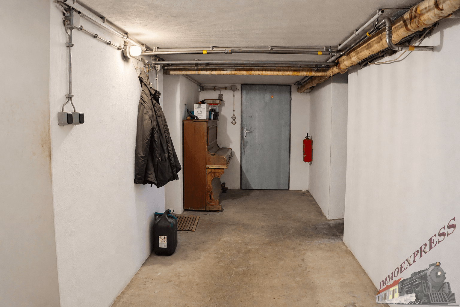 Funktionaler Kellerraum mit sichtbaren Leitungen, Betonboden und einem alten Klavier.