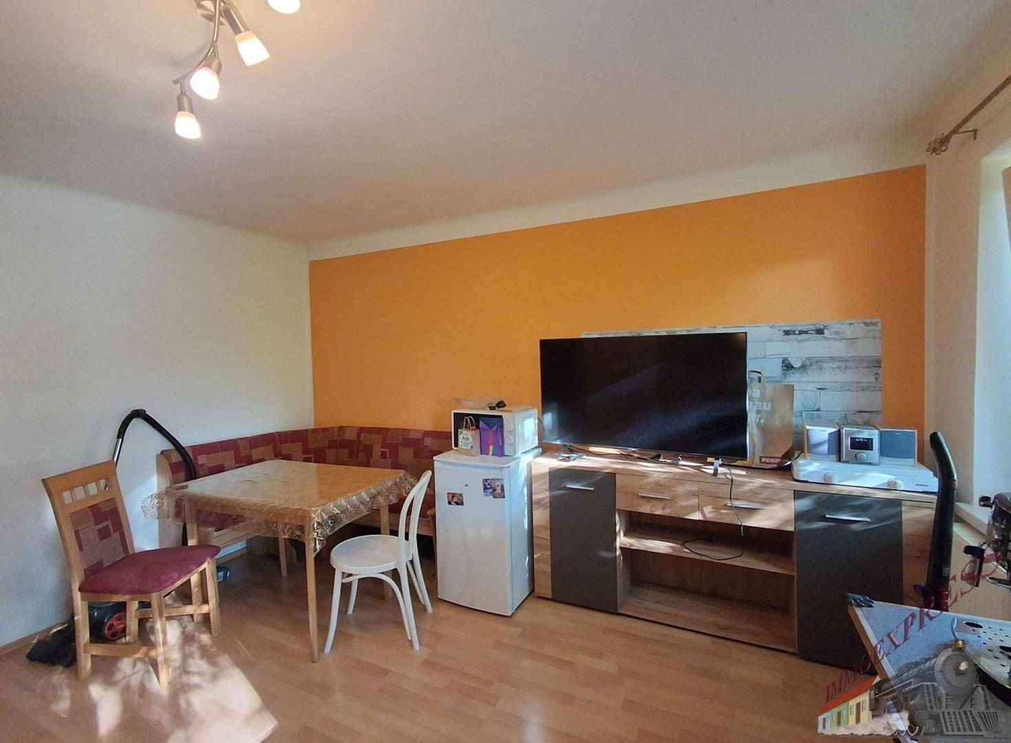 Gemütlicher Wohn- und Essbereich mit orangefarbener Akzentwand, Esstisch und Fernseher.