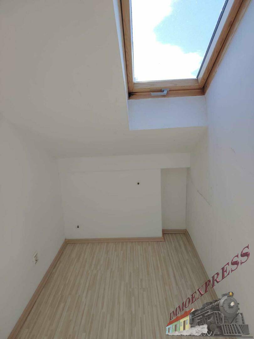 Kleiner Dachgeschossraum mit Laminatboden und einem Dachfenster für helles Tageslicht.