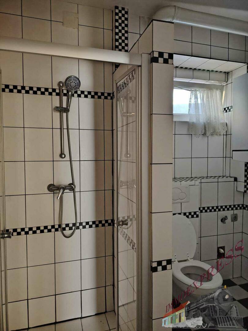 Badezimmer mit Duschkabine, schwarz-weiß karierten Fliesen und einem kleinen Fenster.