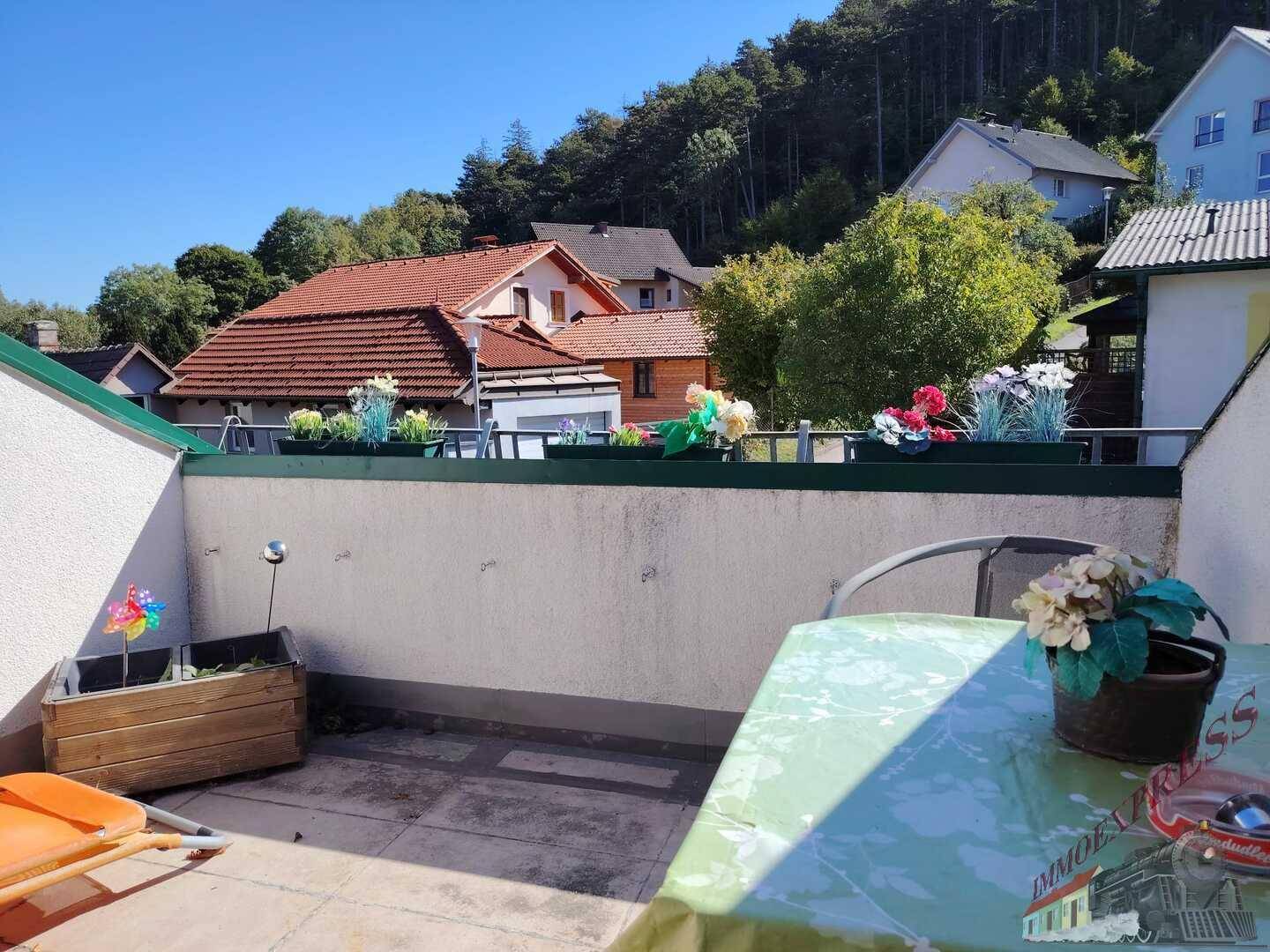 Sonniger Terrassenbereich mit Tisch und Stühlen, umgeben von Blumenkästen und Blick ins Grüne. Entspannende Oase.