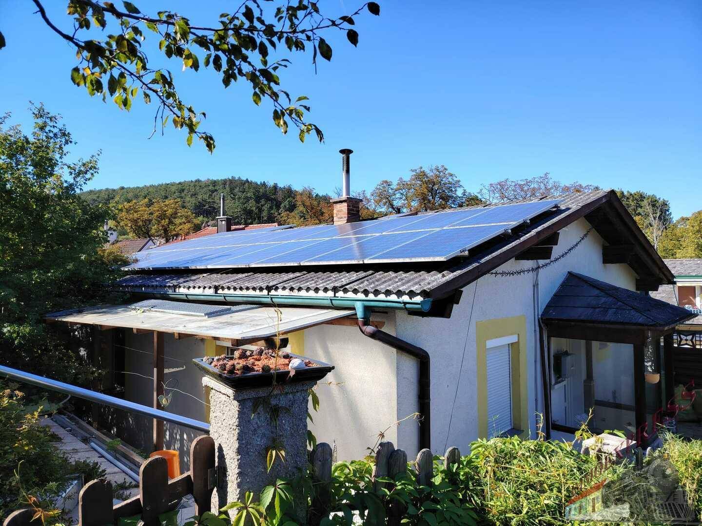 Seitenansicht des Hauses mit Photovoltaikanlage auf dem Dach und umgebender Vegetation. Nachhaltige Energieversorgung.