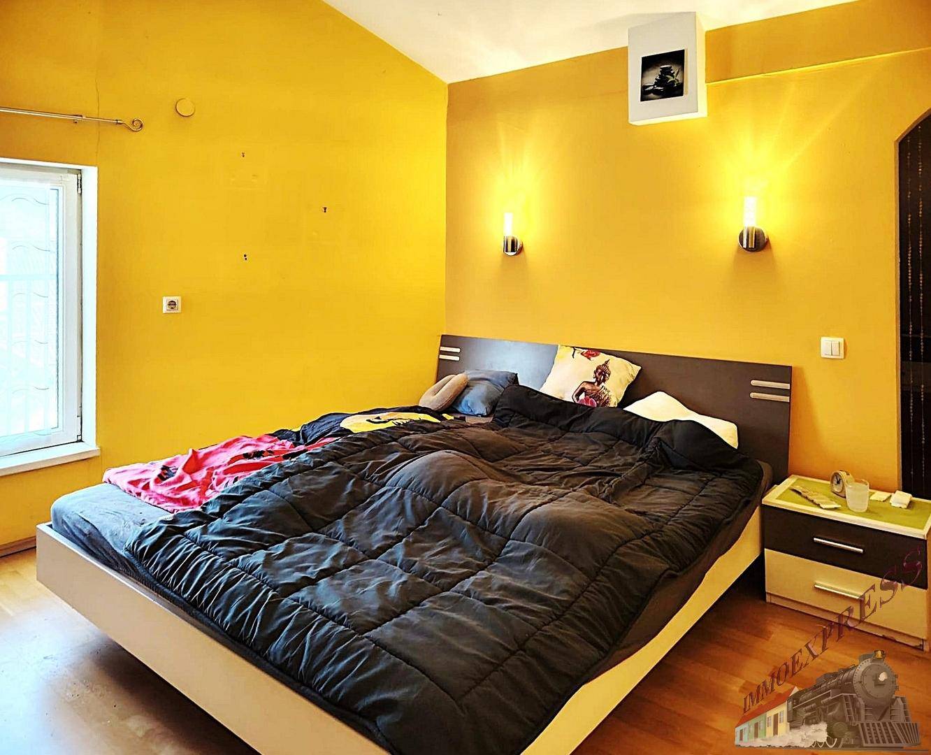 Schlafzimmer mit leuchtend gelben Wänden, Holzboden und einem modernen Doppelbett. Freundliche Atmosphäre.