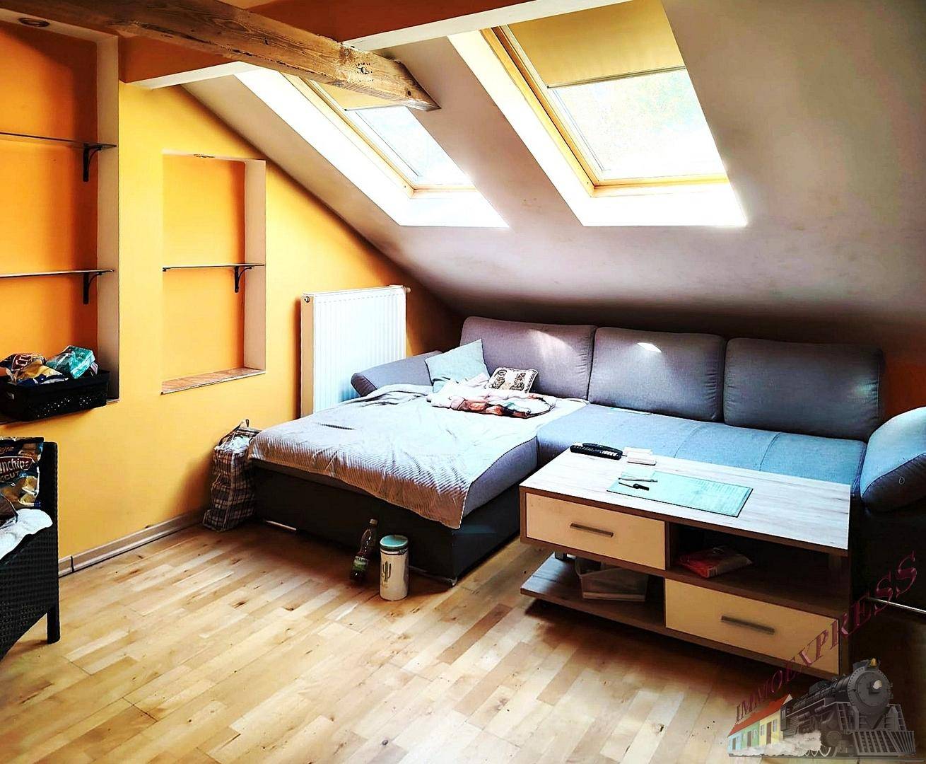 Gemütliches Wohnzimmer im Dachgeschoss mit Schrägdach, Holzbalken und zwei Dachfenstern. Lichtdurchfluteter Raum.