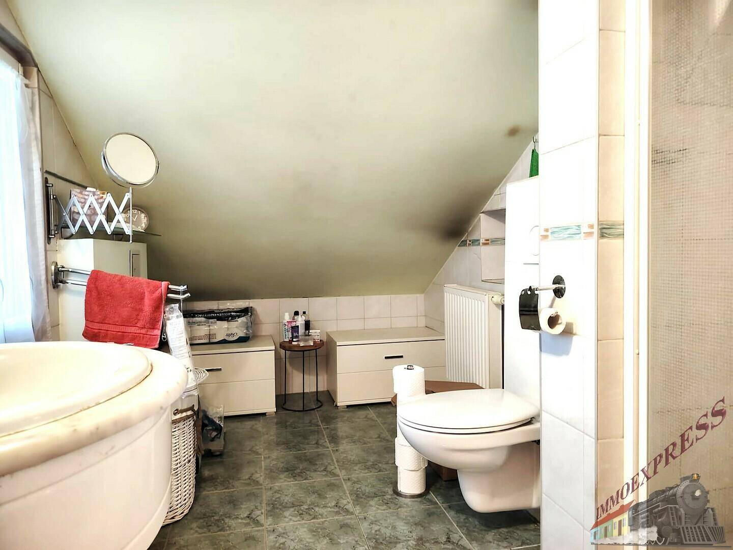 Badezimmer im Dachgeschoss mit Schrägdach, Badewanne, Toilette und Fliesenboden. Praktisch und hell.