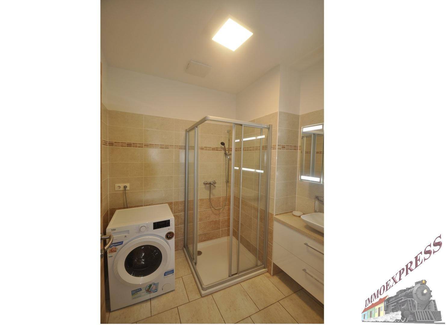Modernes Badezimmer mit Duschkabine, Waschmaschine und hellen Fliesen.