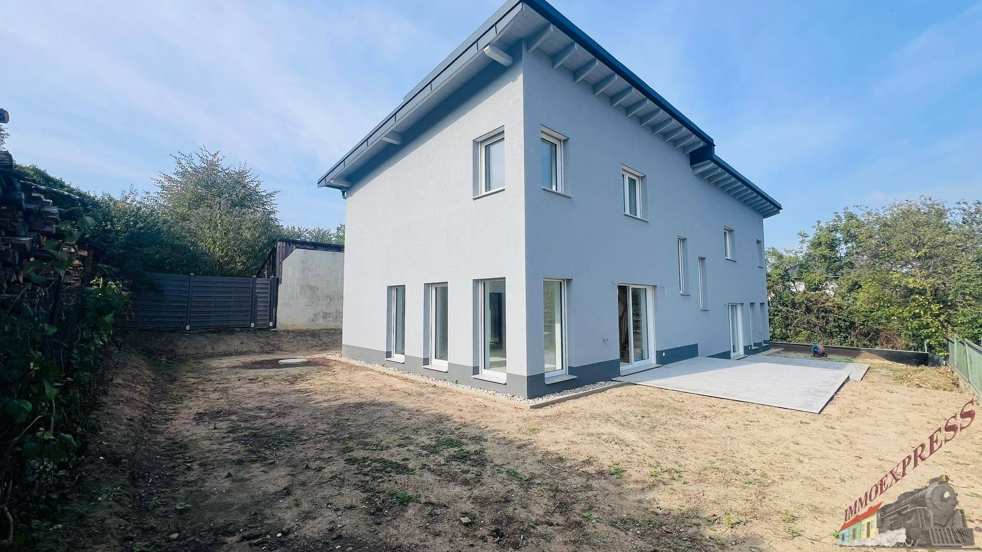 Rückansicht des Neubaus mit großem Gartenbereich und einer vorbereiteten Terrasse.