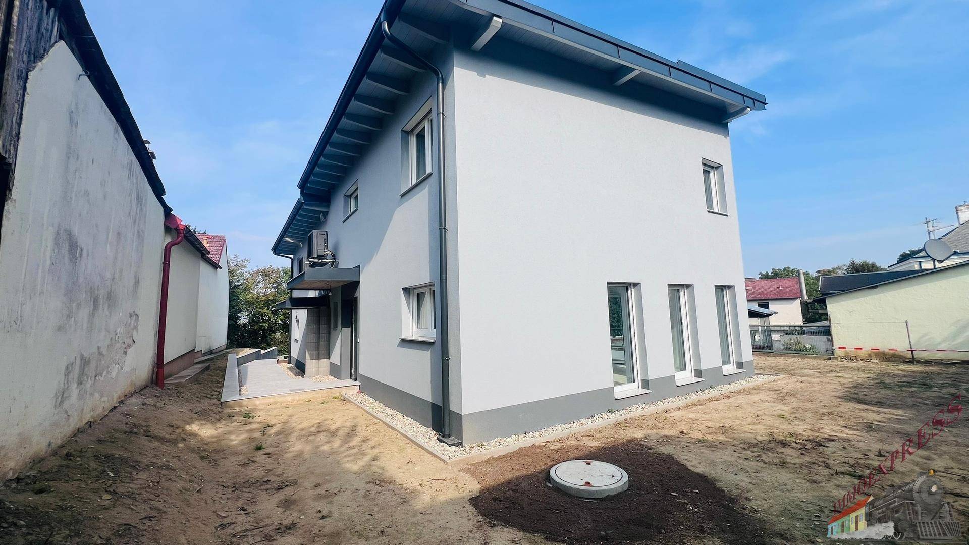 Seitenansicht des Hauses mit grauem Anstrich und unfertigem Gartenbereich.