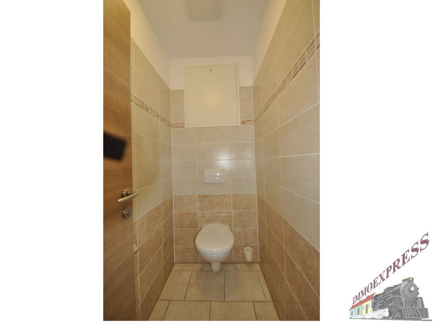 Separate Toilette mit Wand-WC und beigefarbenen Fliesen an Wänden und Boden.