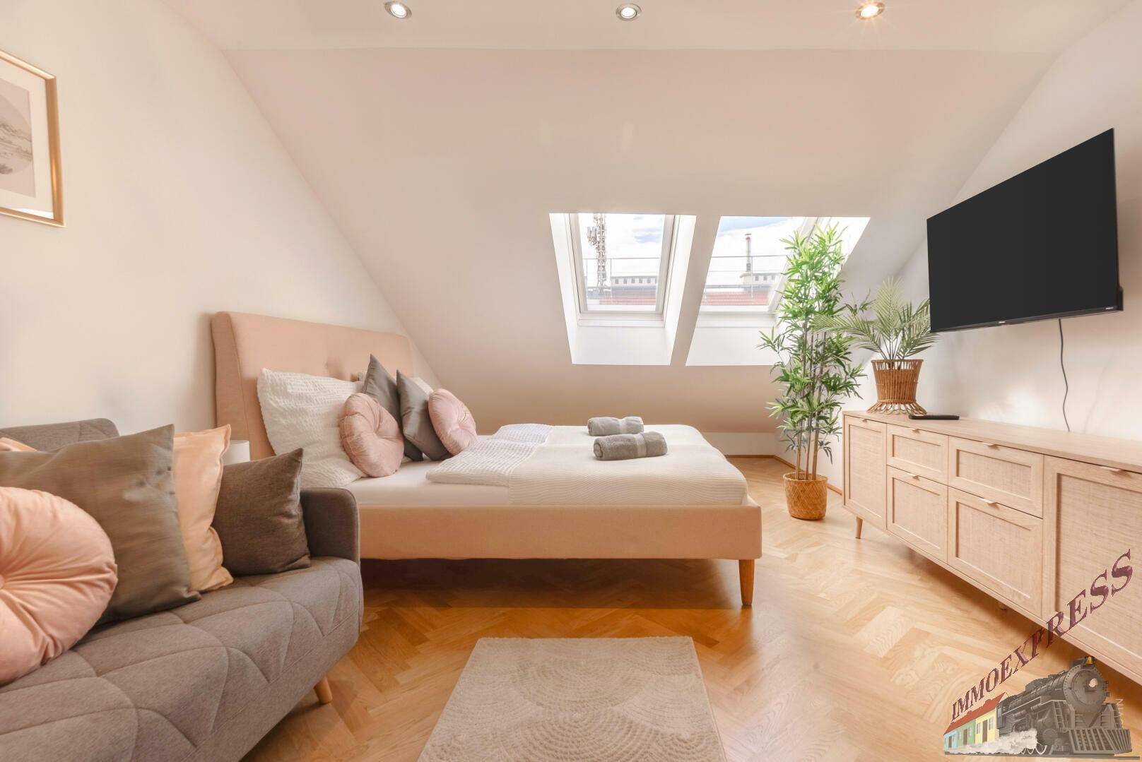 Helles Schlafzimmer im Dachgeschoss mit Dachfenstern, TV und Holzboden.