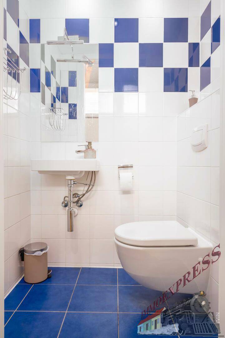 Separates WC mit Wand-WC, Waschbecken und blau-weißen Fliesen.