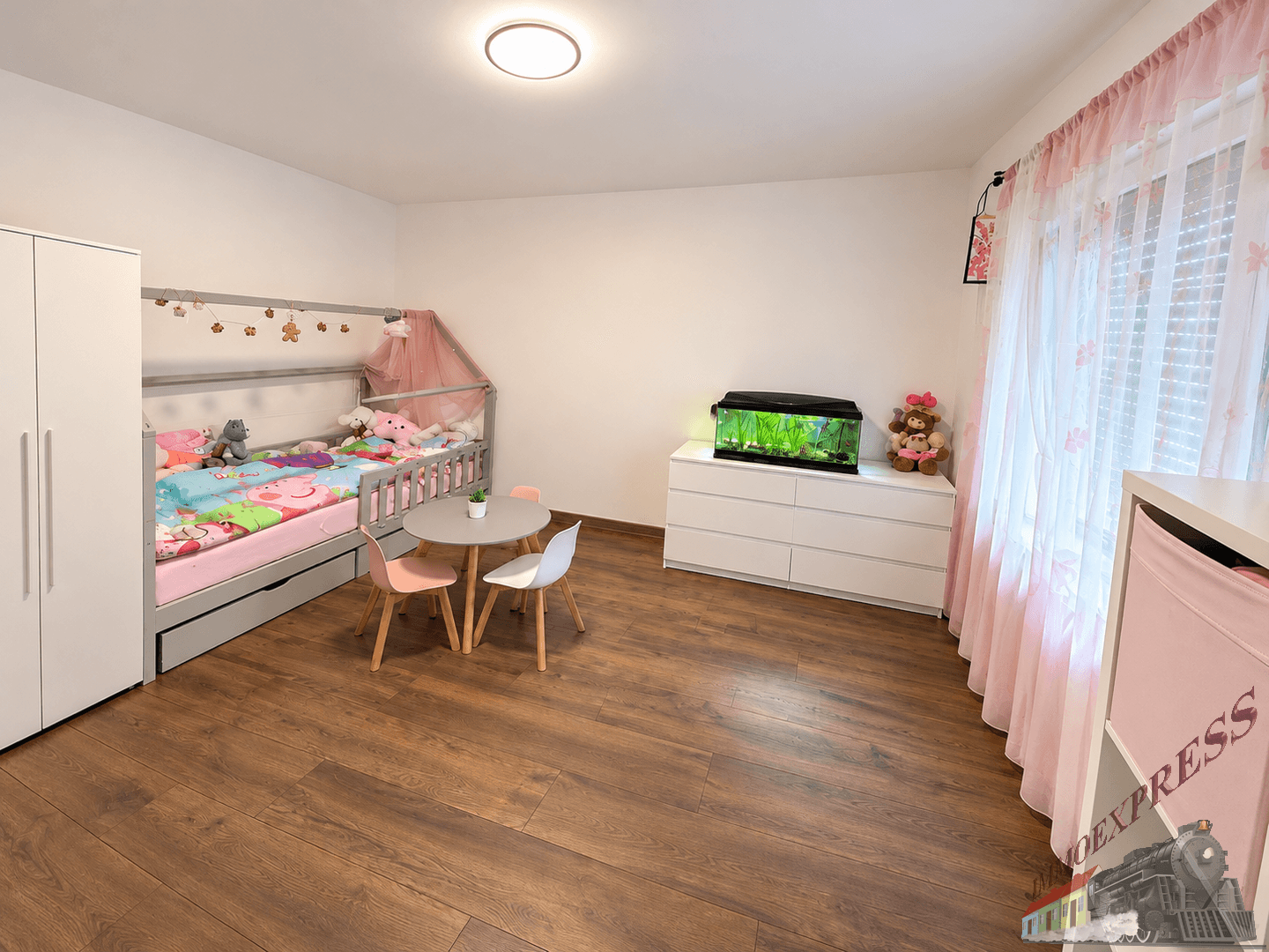 Kinderzimmer mit Holzboden, kleinem Tisch und Bett mit rosa Dekoration.