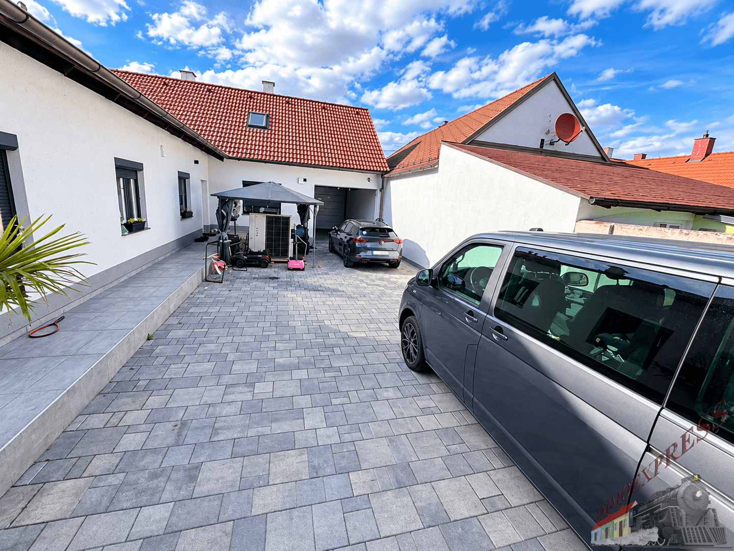 Gepflasterte Einfahrt mit Parkplätzen für mehrere Fahrzeuge und Zugang zur Garage.