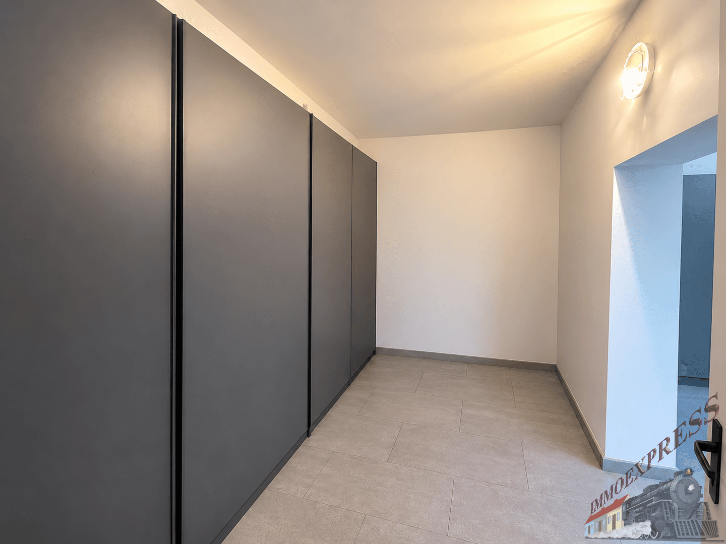 Heller Raum mit grauen Einbauschränken und Fliesenboden, möglicherweise ein Flur oder Ankleidezimmer.