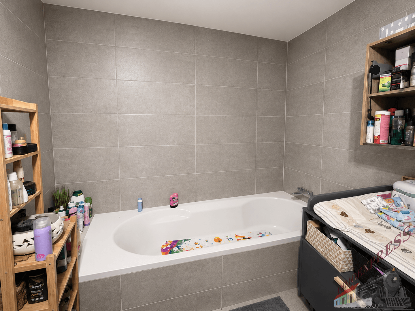 Badezimmer mit Badewanne, grauen Wandfliesen und Holzregalen für Utensilien.
