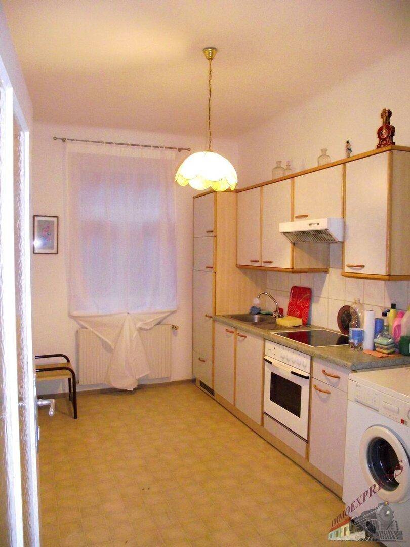 Helle Küche mit Fenster, weißen Schränken, Herd und Waschmaschine, gut beleuchtet.