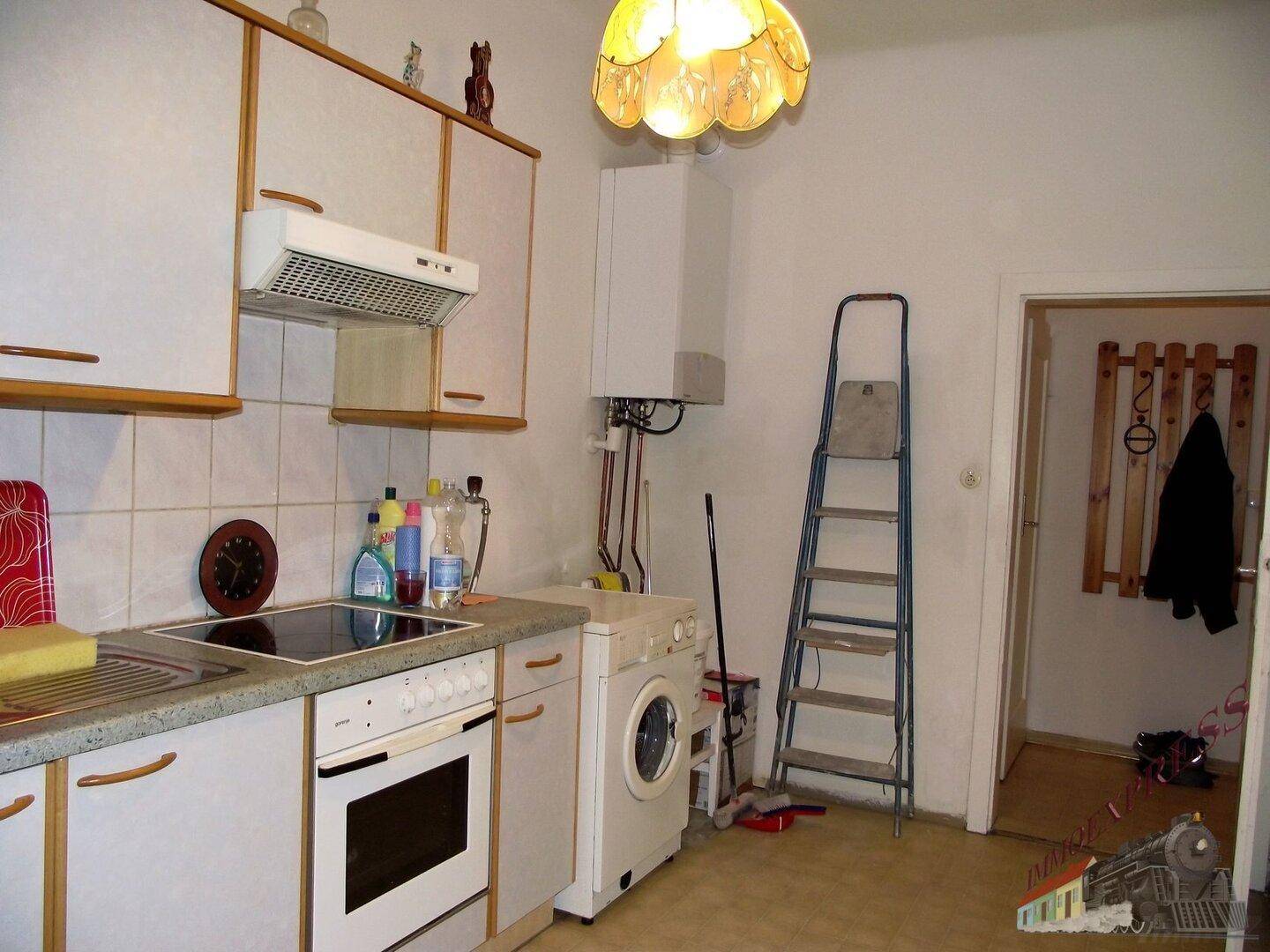 Ältere Einbauküche mit weißen Schränken, Herd und Waschmaschine, funktional ausgestattet.