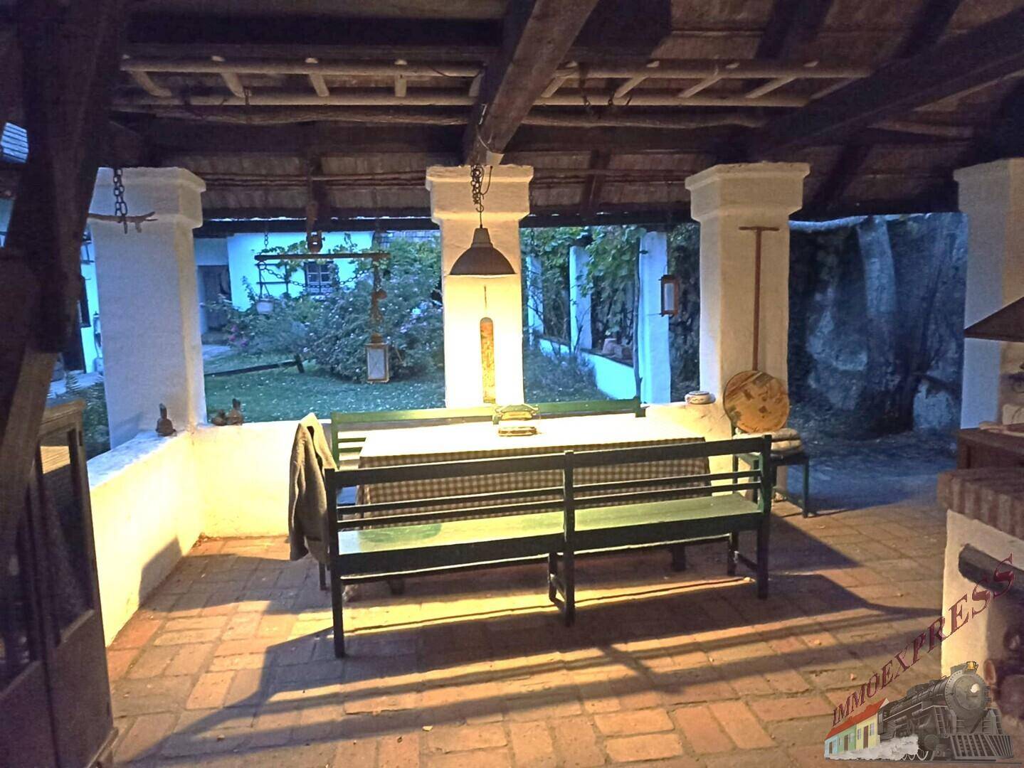 Beleuchtete überdachte Terrasse am Abend mit Sitzbänken und Blick in den Garten.