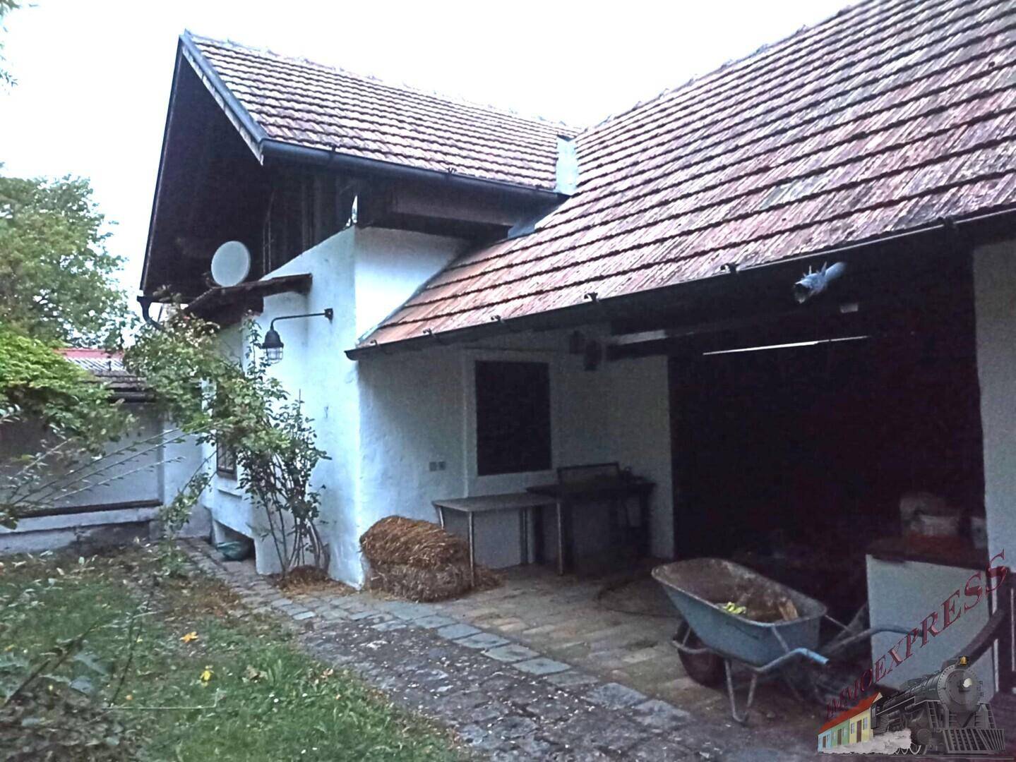 Seitenansicht eines ländlichen Gebäudes mit Ziegeldach und offenem Unterstand.