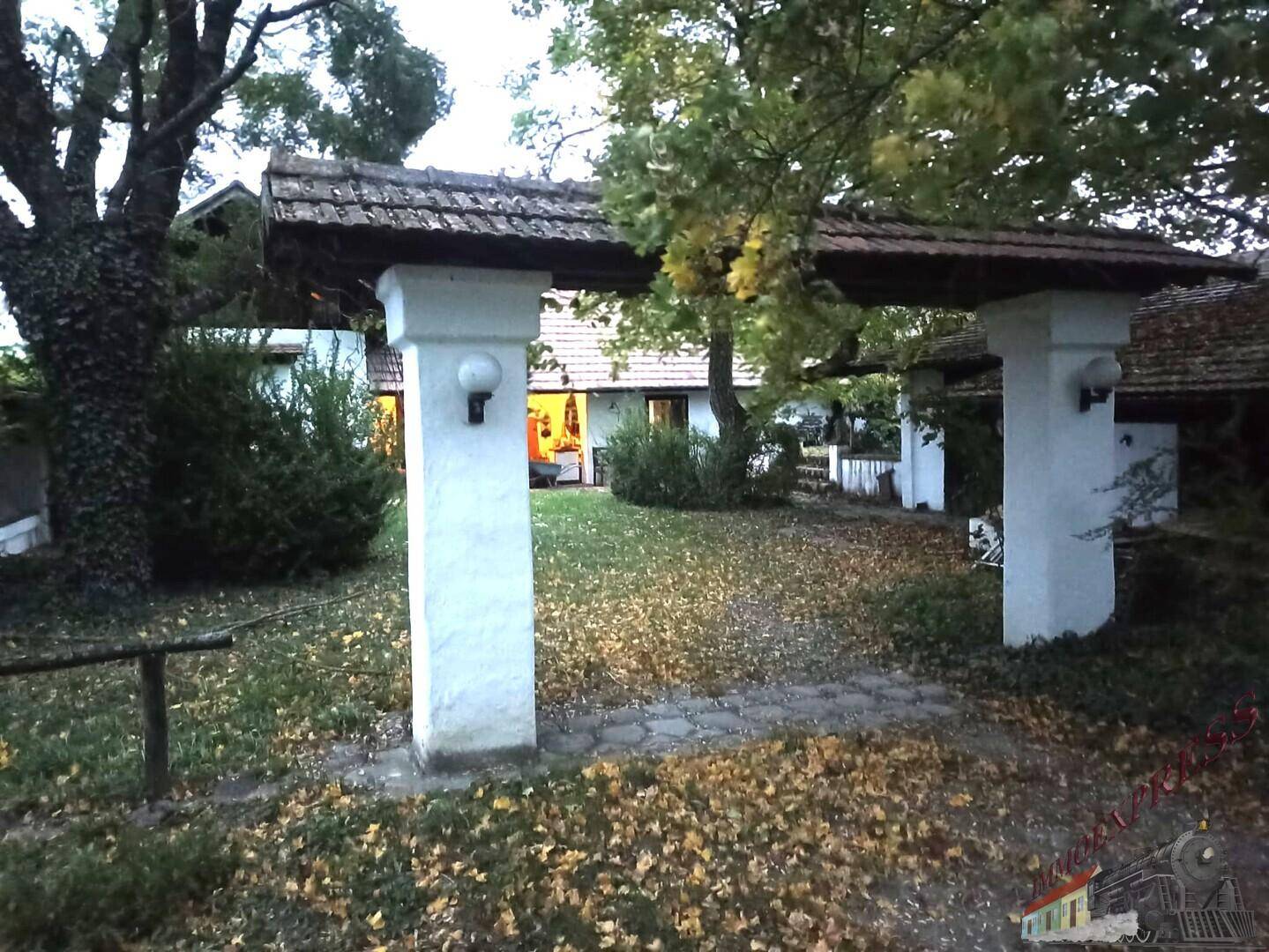 Eingangsbereich zum Garten mit überdachtem Torbogen und Herbstlaub auf dem Rasen.