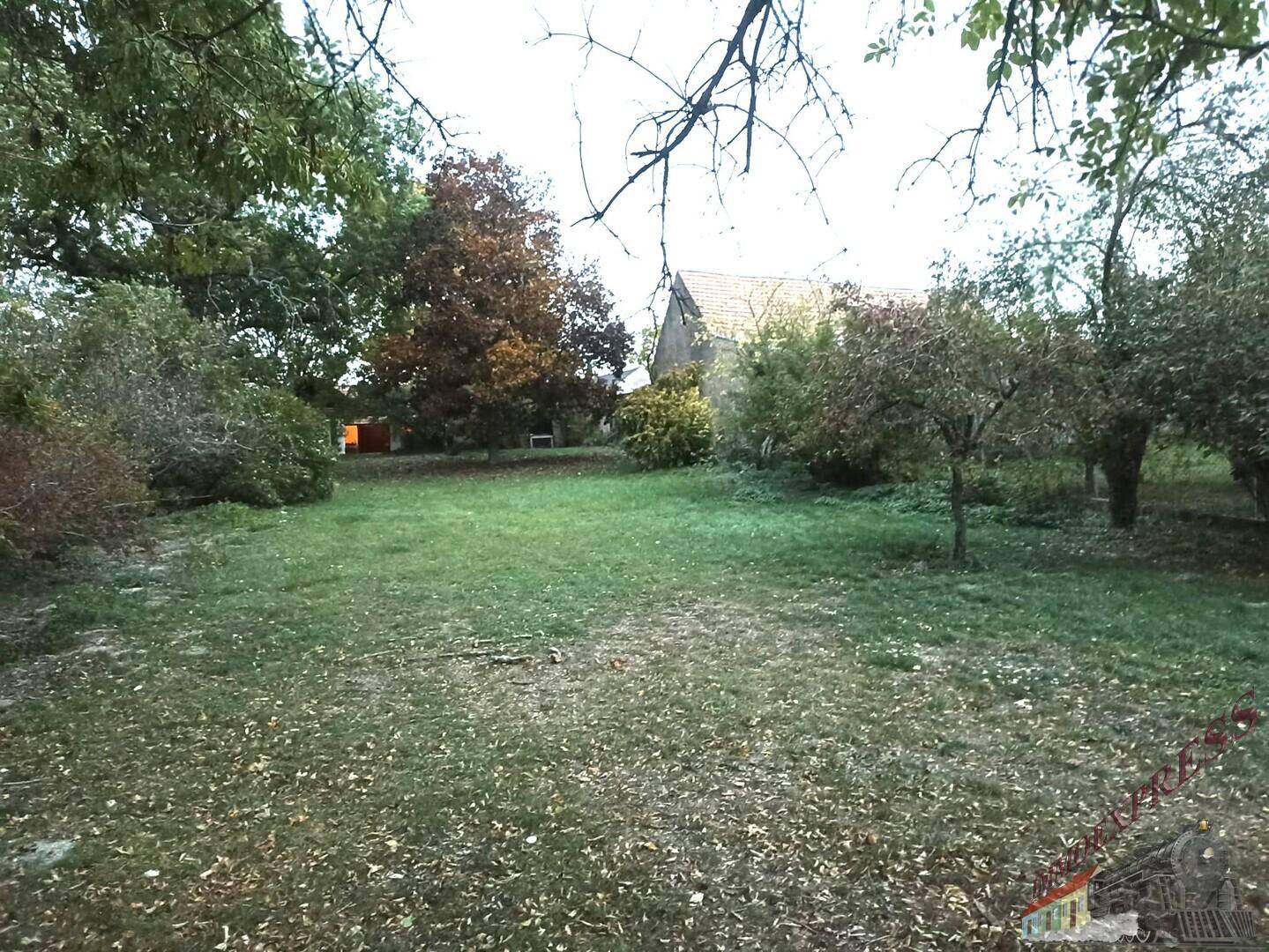 Großer Gartenbereich mit Rasen, verschiedenen Bäumen und ländlichem Haus im Hintergrund.