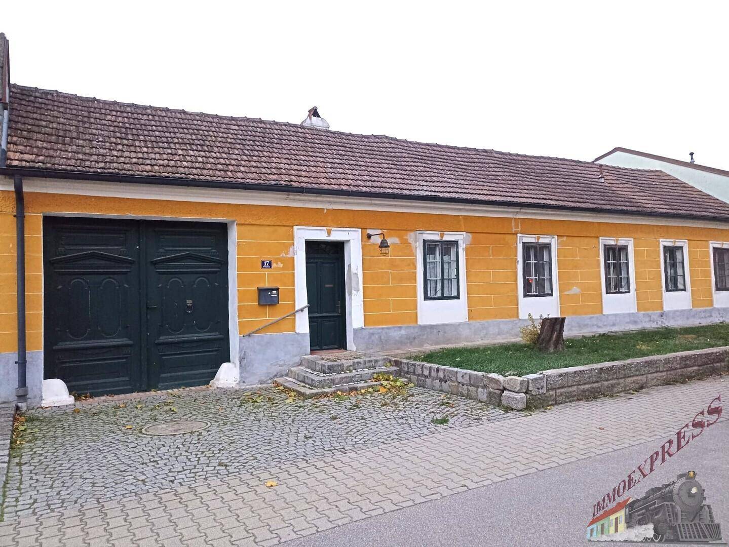 Traditionelles Gebäude mit gelber Fassade, Ziegeldach und gepflasterter Einfahrt.