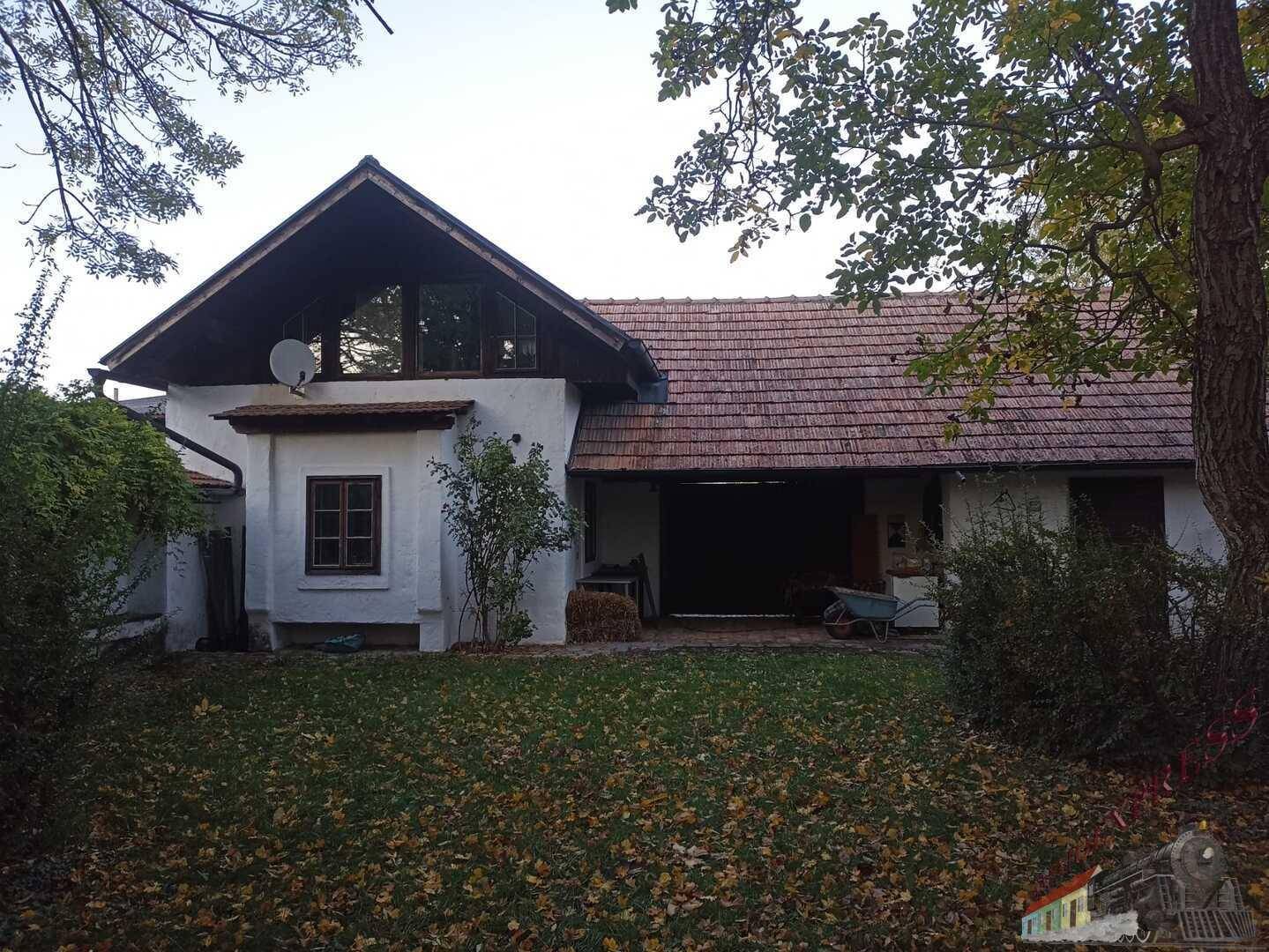 Ländliches Haus mit Ziegeldach und großem Gartenbereich, umgeben von Bäumen.