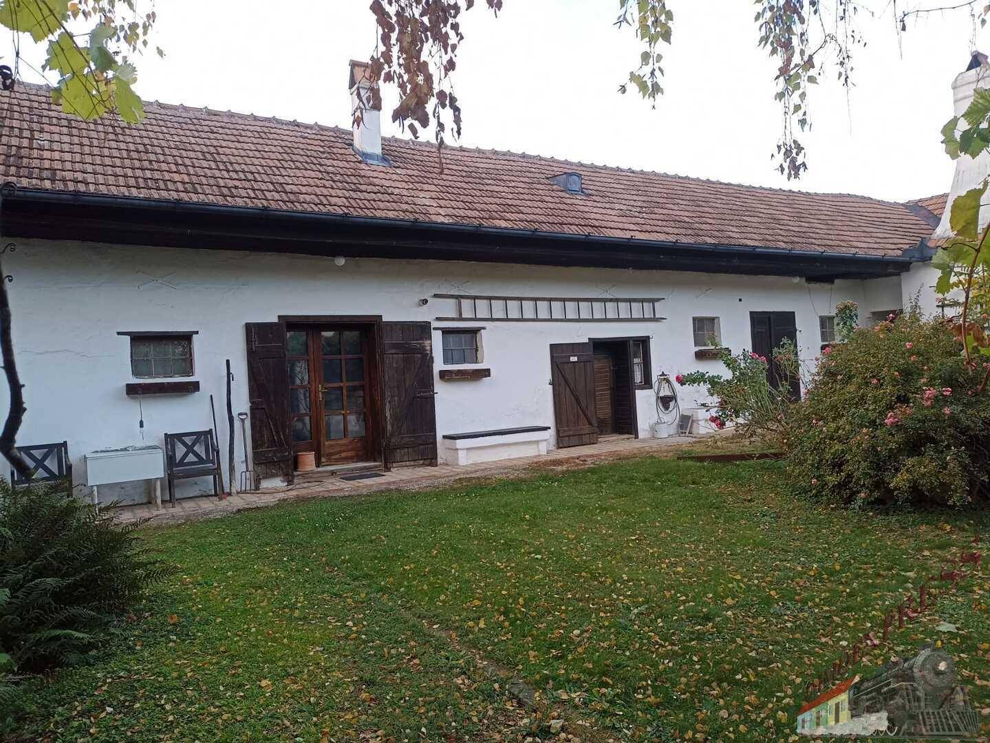 Rückseite eines ländlichen Hauses mit Garten, Holzfensterläden und Leiter an der Wand.