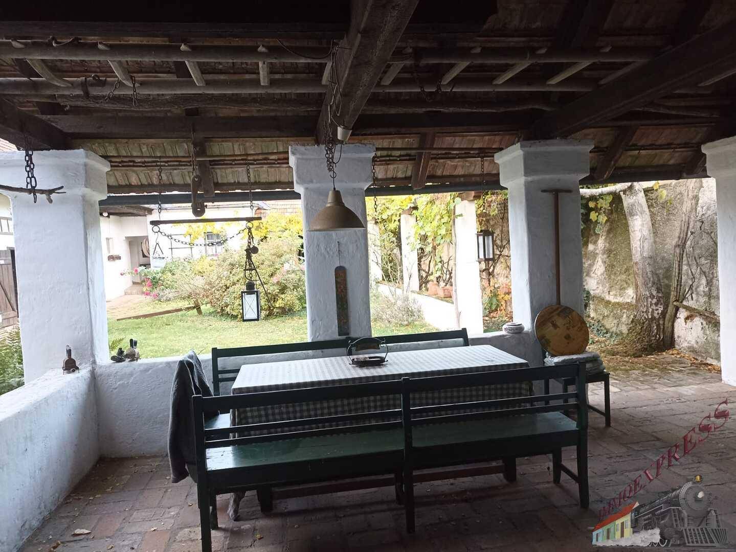 Überdachte Terrasse mit Holzbalken, Sitzbänken und Blick in den Garten.