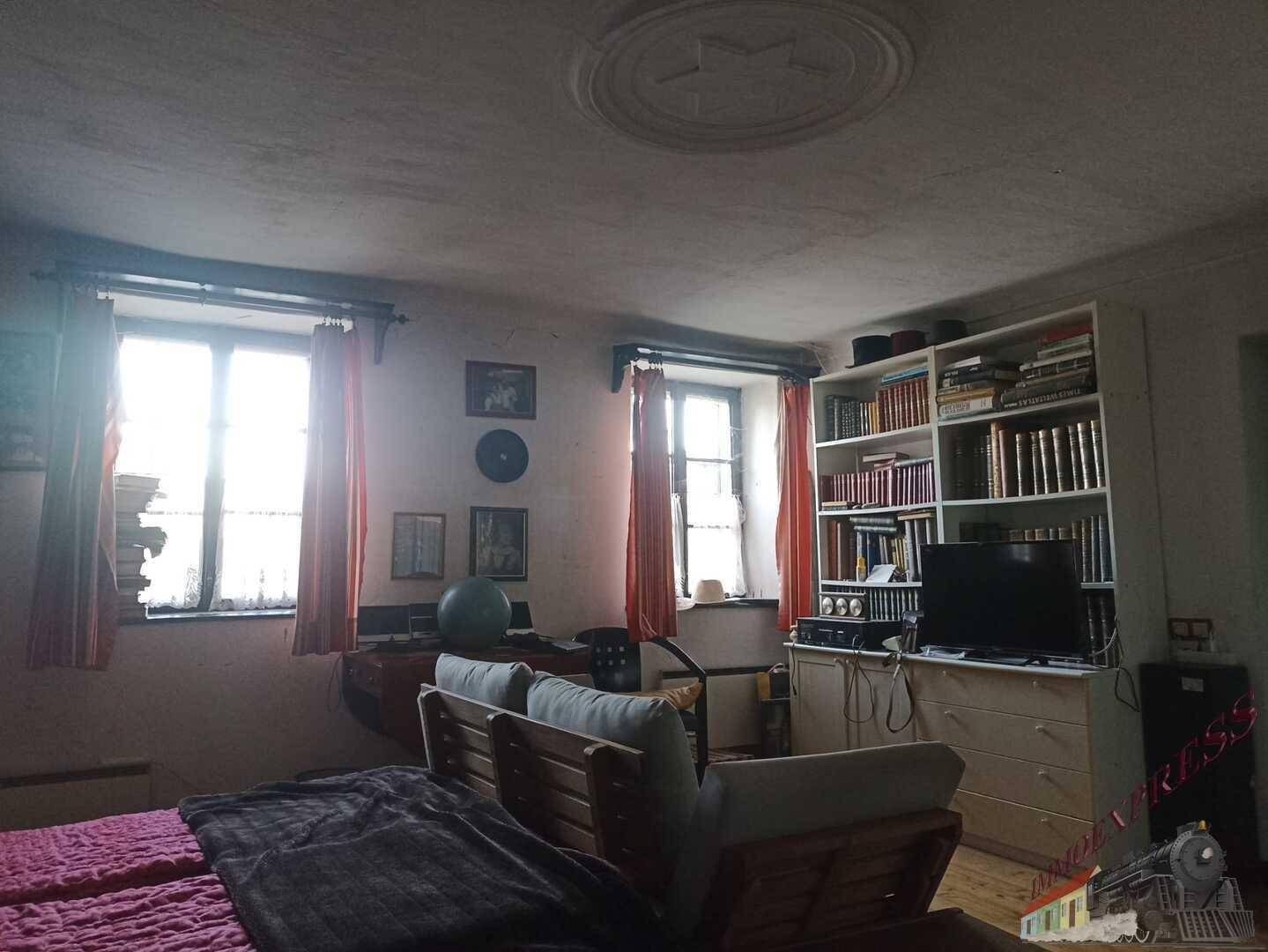 Helles Schlafzimmer mit zwei Fenstern, Bücherregal und Sofa.