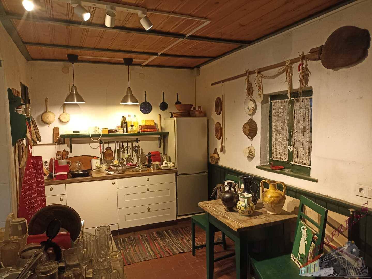 Rustikale Küche mit Holzbalkendecke, einfachen weißen Schränken und Esstisch.