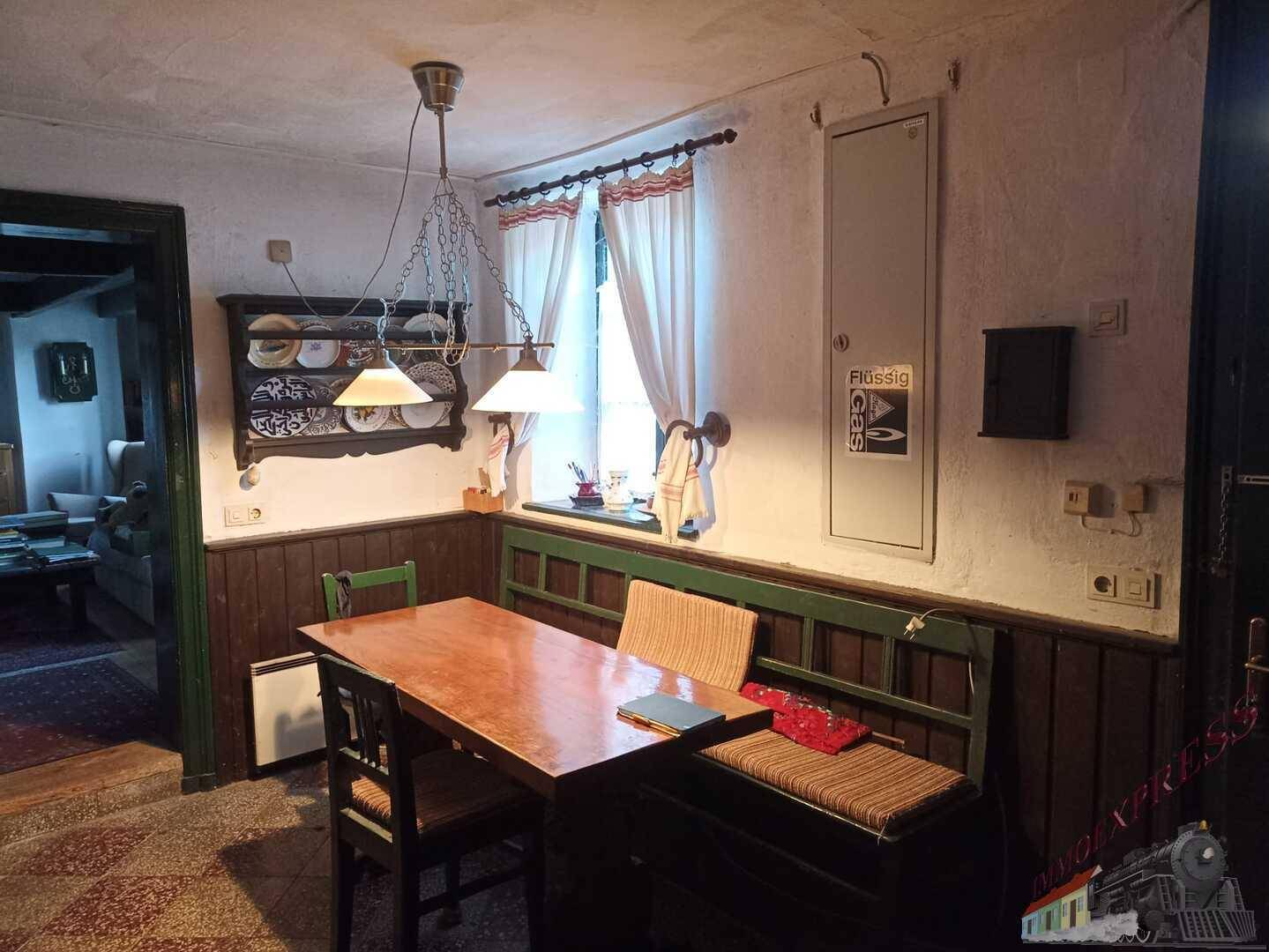 Gemütlicher Essbereich mit Holztisch, Sitzbank und Fenster mit Vorhängen.