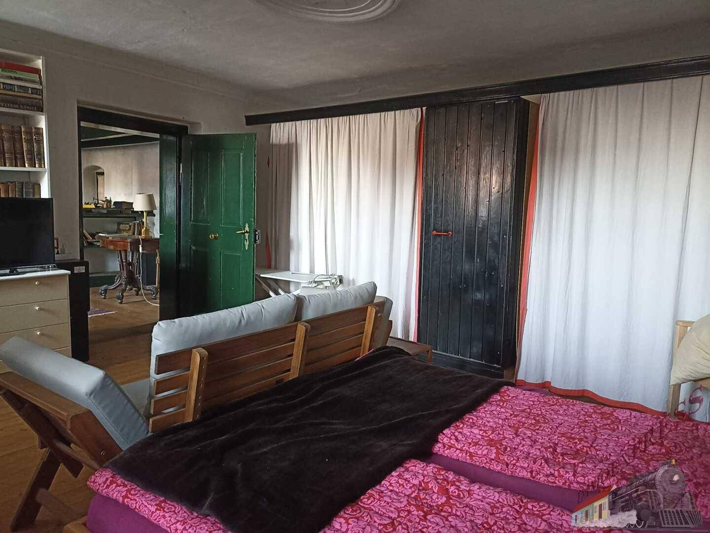 Schlafzimmer mit Holzboden, Sofa und Blick in einen angrenzenden Raum.