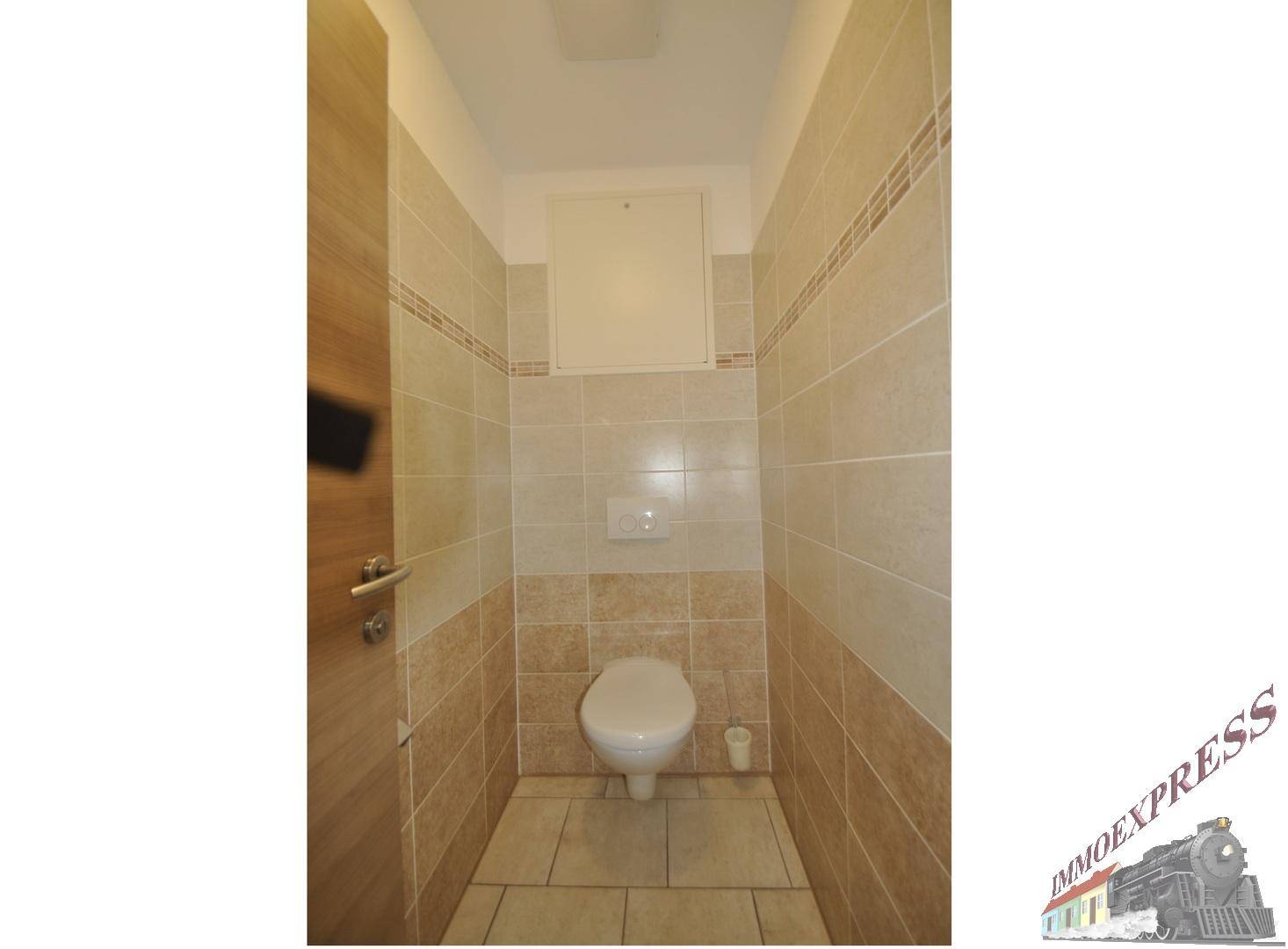 Separate Toilette mit beigefarbenen Fliesen und wandmontiertem WC, in einem schmalen Raum.