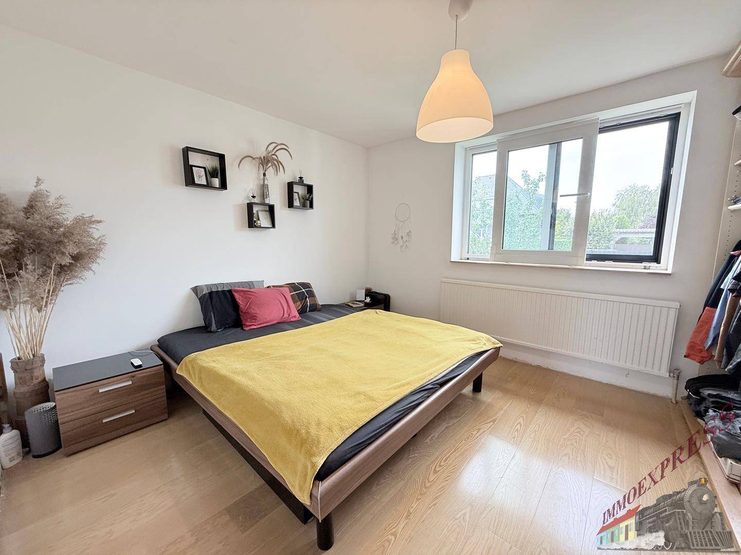 Helles Schlafzimmer mit Holzboden, Doppelbett und einem Fenster mit Blick ins Grüne.