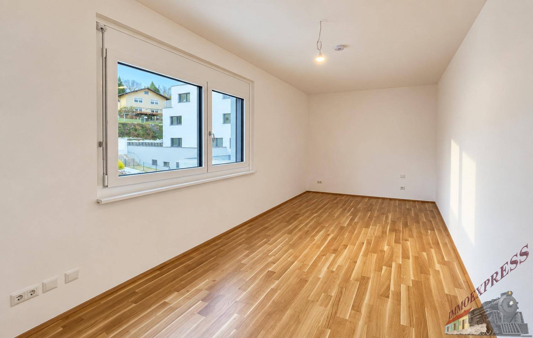 Geräumiges Schlafzimmer mit Parkettboden und großem Fenster mit Blick ins Grüne.