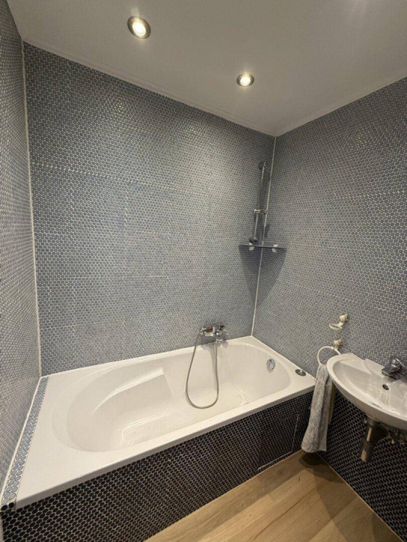 Badezimmer mit Badewanne, integrierter Dusche und modernen Mosaikfliesen an den Wänden.