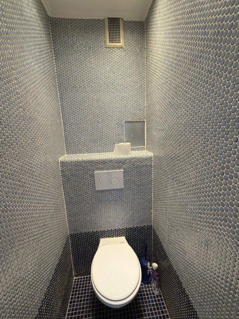 Modernes Gäste-WC mit auffälligen Mosaikfliesen an den Wänden und einem Wand-WC.