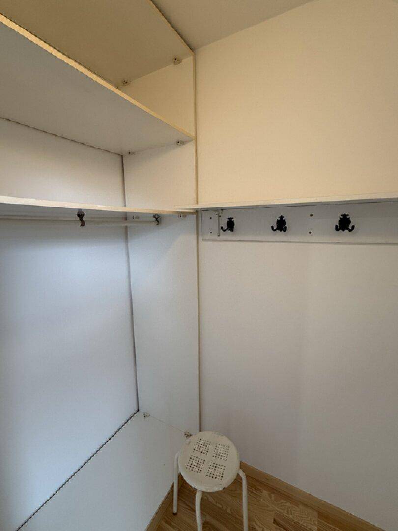 Kleiner begehbarer Kleiderschrank mit praktischen Regalen und Haken für Kleidung.