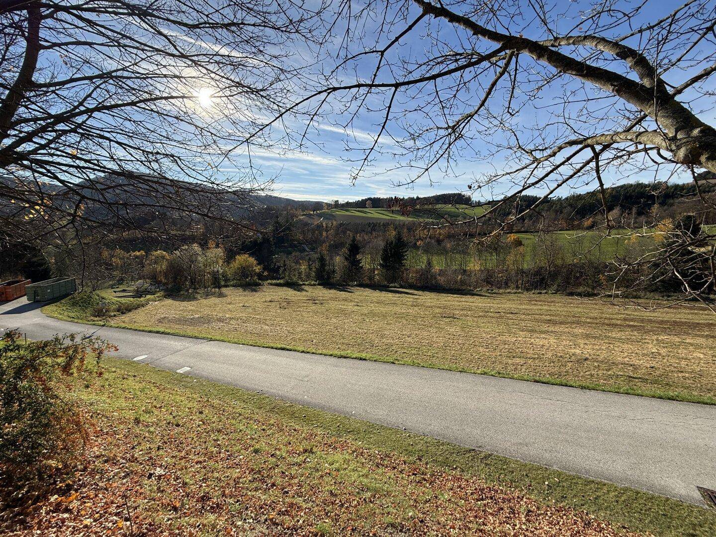 Weitläufiger Blick über ein Feld und die umliegende Natur, mit einer Straße im Vordergrund.