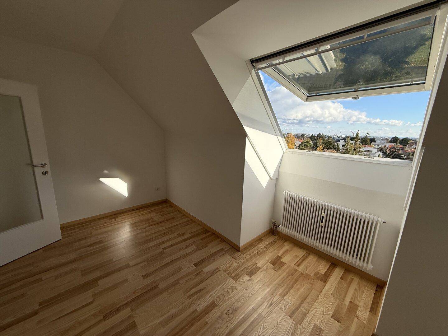 Leeres Schlafzimmer im Dachgeschoss mit Holzboden, Dachfenster und viel Tageslicht.