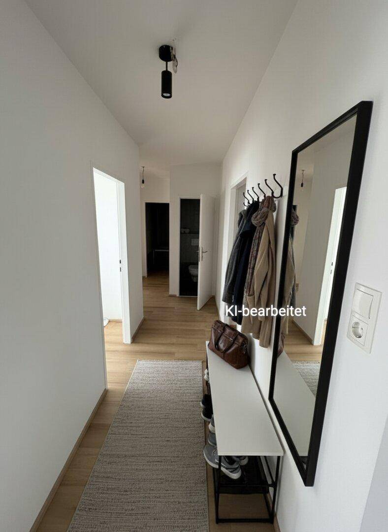 Heller Flur mit Holzfußboden, Garderobe und großem Spiegel, der in weitere Räume führt.