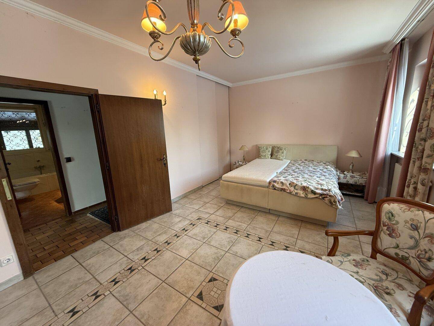 Schlafzimmer mit Doppelbett und Zugang zu einem angrenzenden Badezimmer mit Fliesenboden.