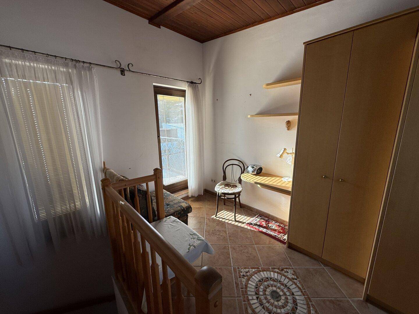Dachgeschosszimmer mit Holzbalkendecke, Fliesenboden und Kleiderschränken und Fenster.