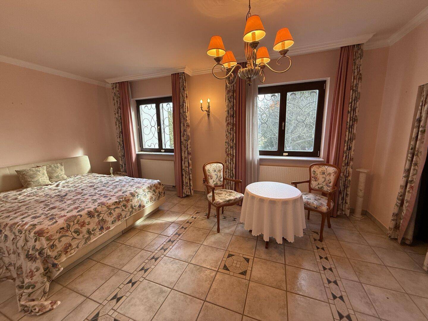 Geräumiges Schlafzimmer mit Fliesenboden, Doppelbett und zwei Fenstern.