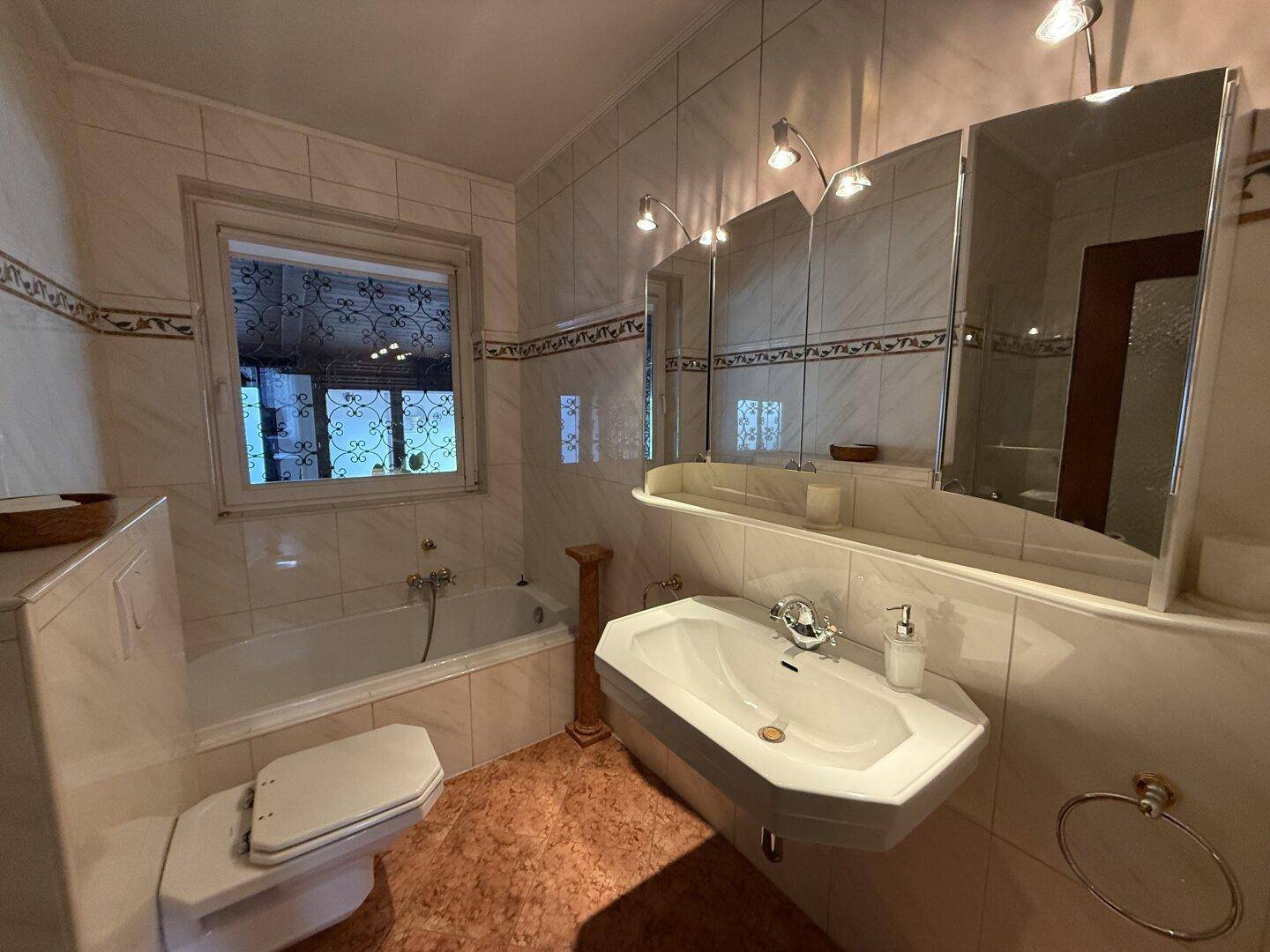 Badezimmer mit Badewanne, Einzelwaschbecken und Fenster, gefliest in hellen Tönen.