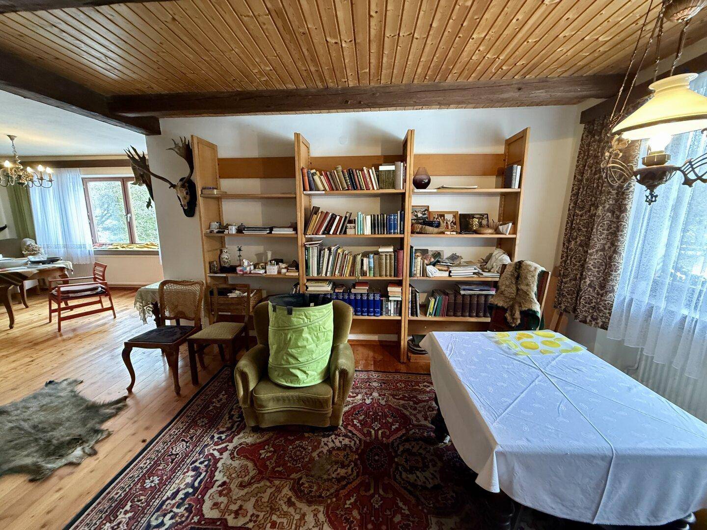 Gemütlicher Wohn- und Essbereich mit Holzdecke, Bücherregal und traditionellen Möbeln.