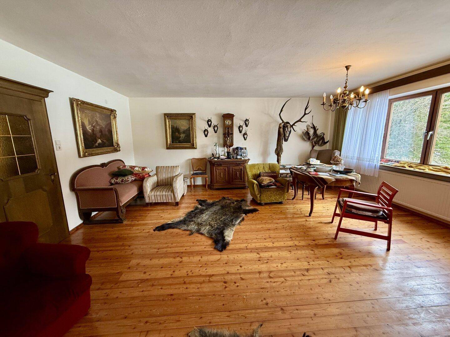 Geräumiges Wohnzimmer mit Holzdielenboden, traditionellen Möbeln und Jagdtrophäen an den Wänden.