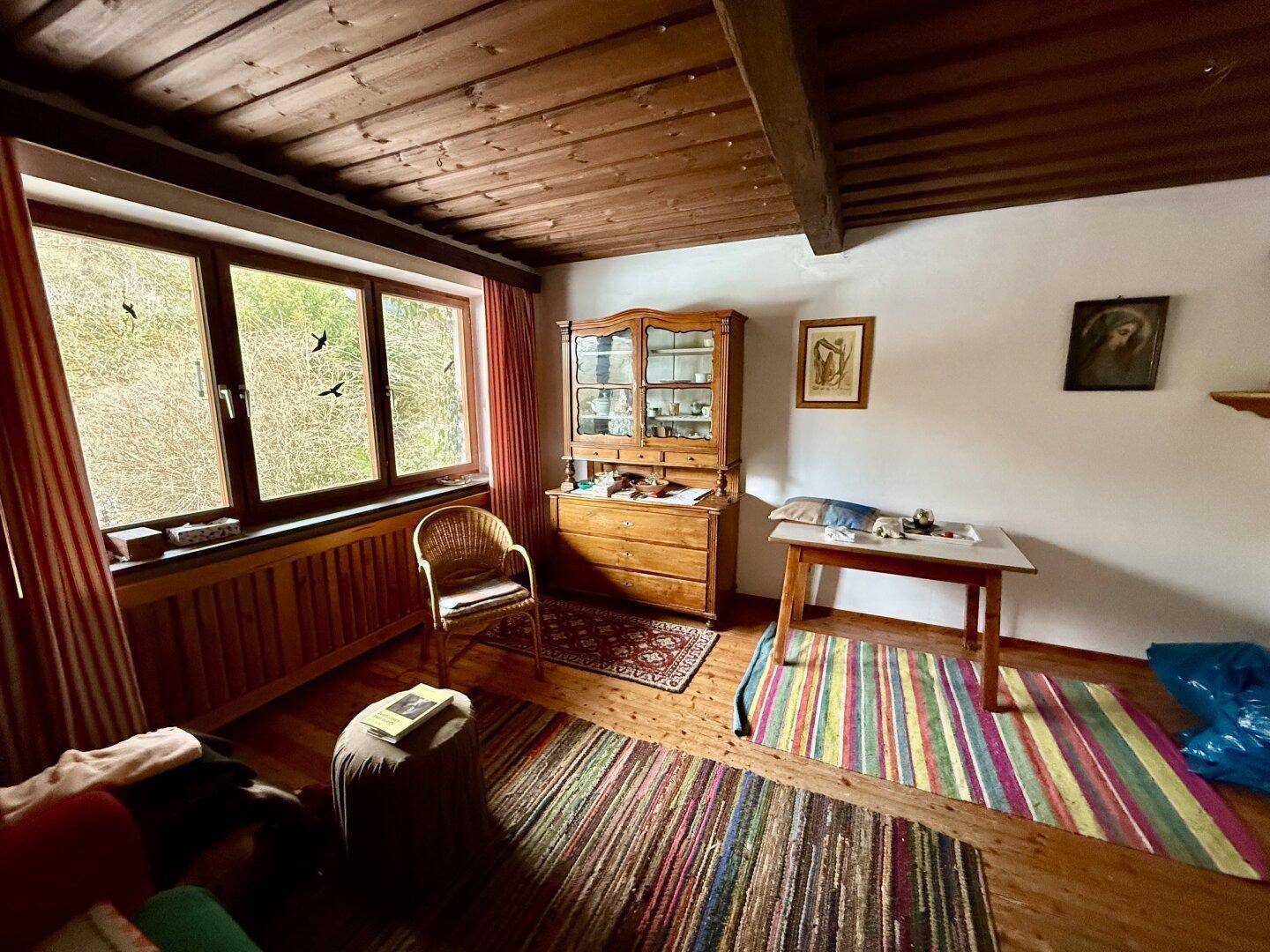Helles Zimmer mit Holzbalkendecke, bunten Teppichen und Blick ins Grüne.